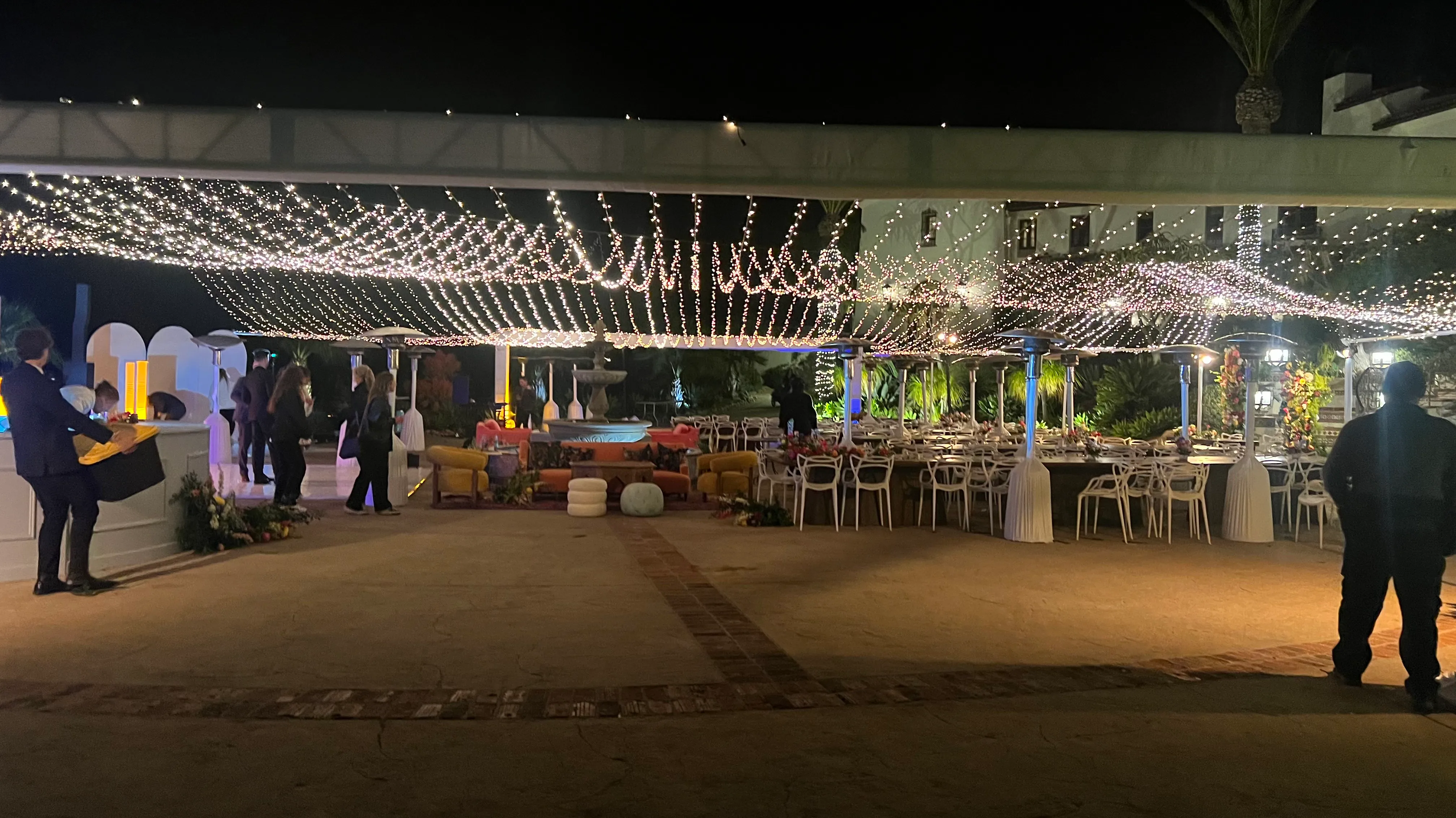 Warm twinkle light canopy installed over a courtyard dinner with tables set beneath the lights